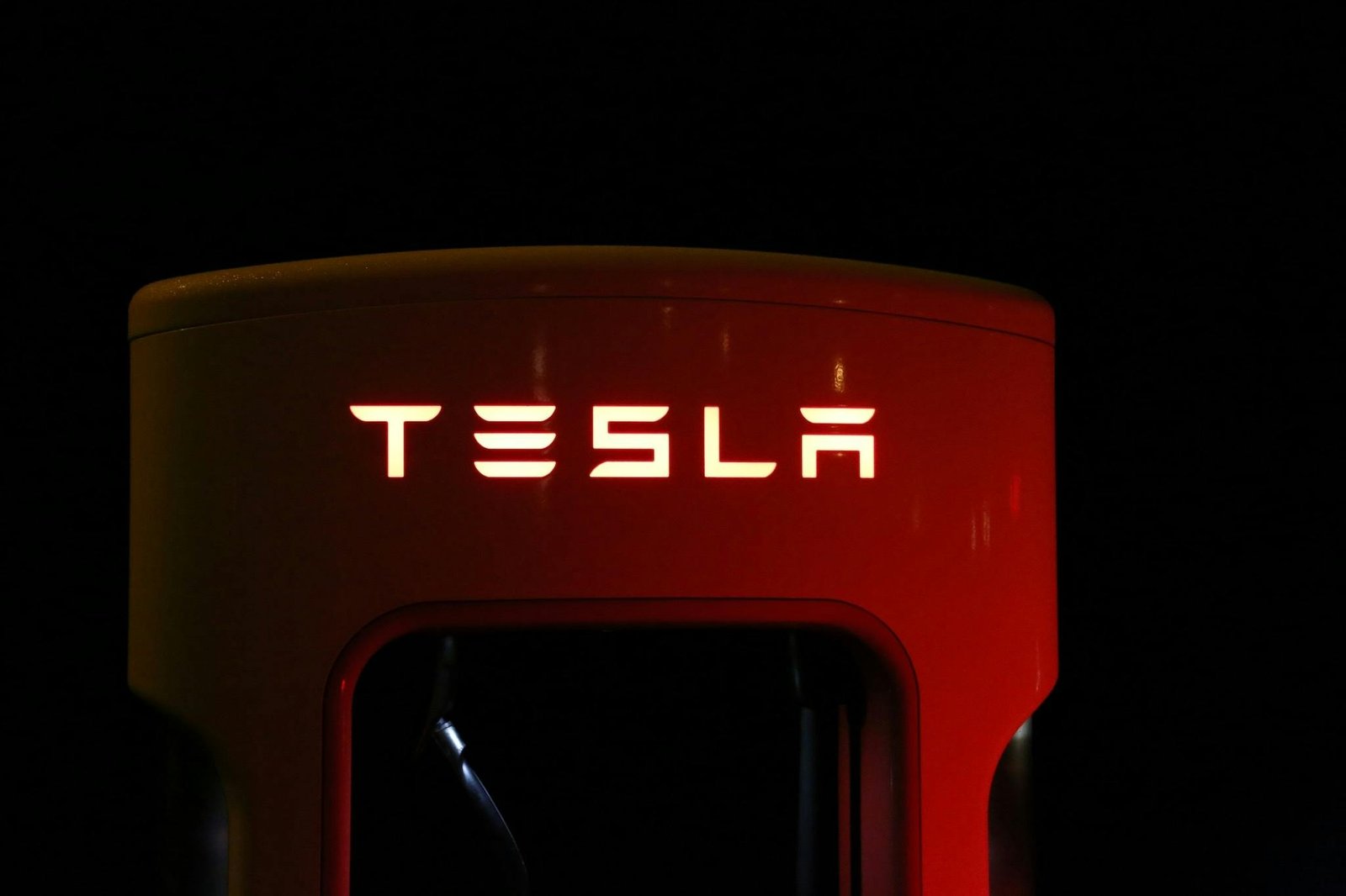 Close-up of a Tesla charging station illuminated at night, showcasing modern automotive technology.