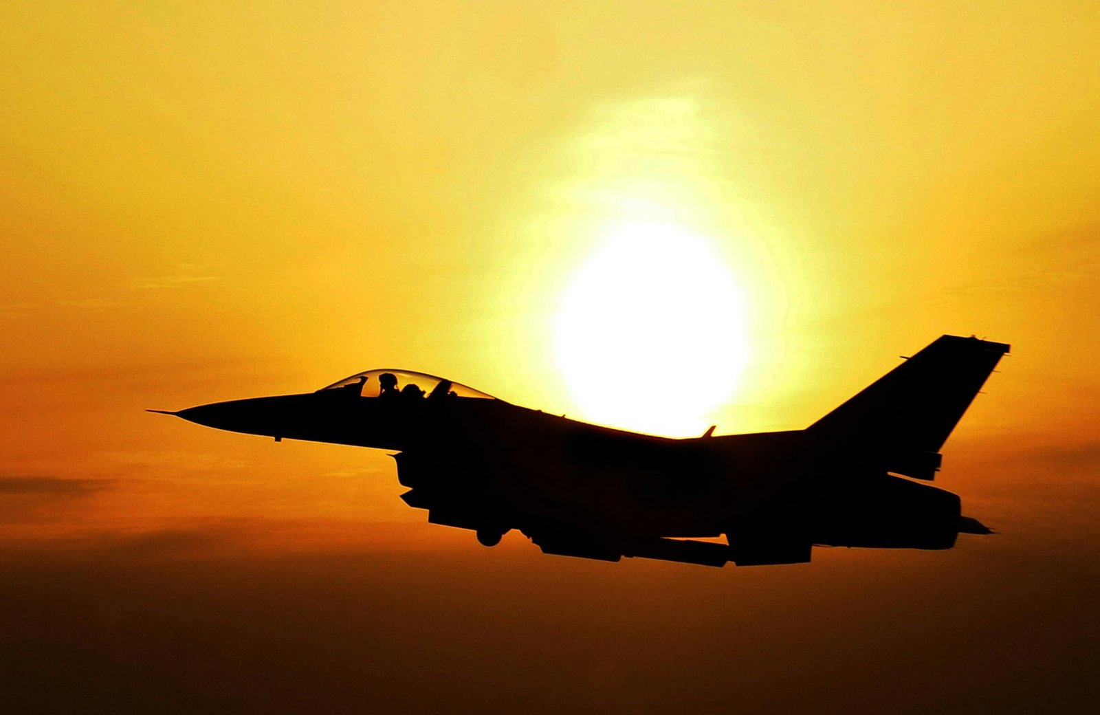 Silhouette of a fighter jet flying during sunrise, highlighting aviation and defense themes.