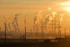 Silhouette of power lines and industrial smoke at sunset, highlighting pollution and energy themes.