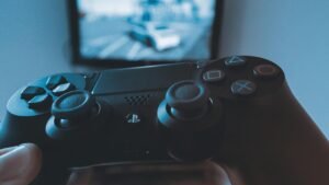 A hand holding a wireless game controller in front of a blurry screen, capturing the gaming experience.