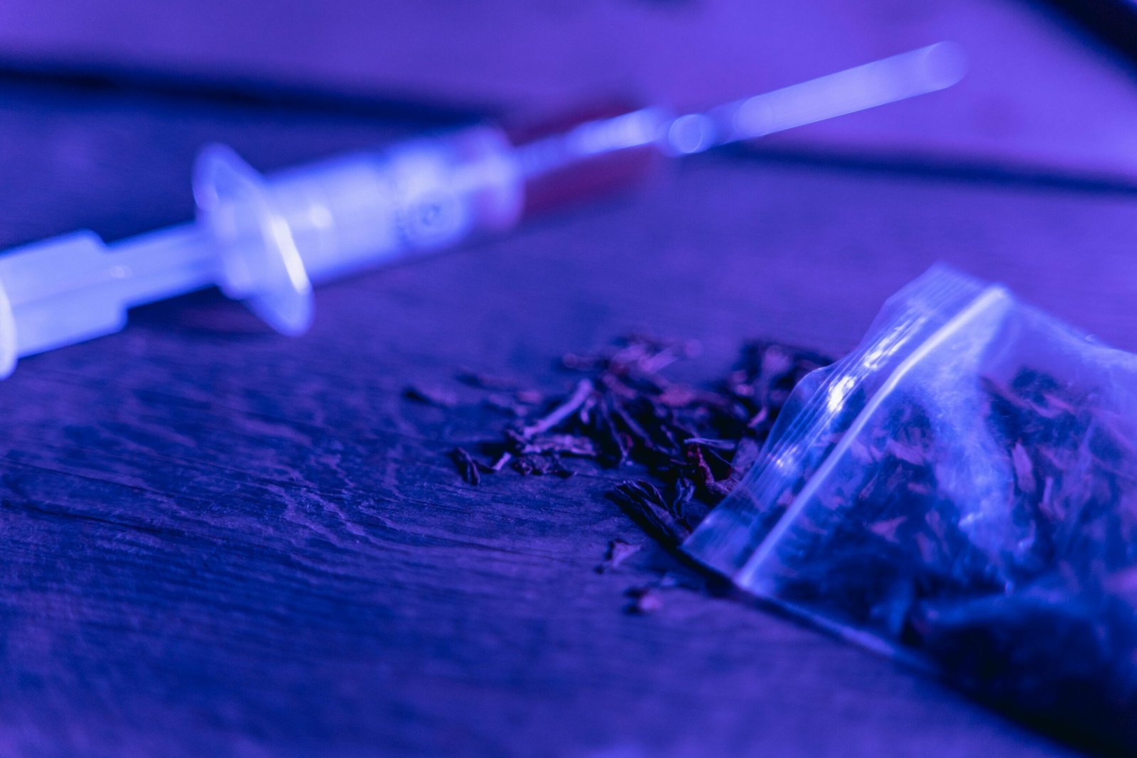 Close-up of a syringe and a bag of dried substance with blue lighting.